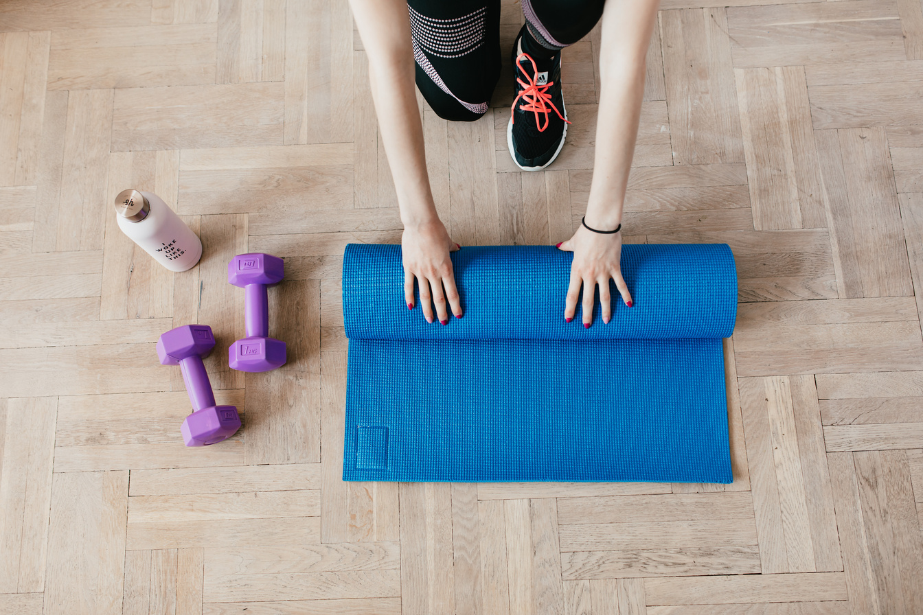 Crop sportswoman unfolding sport mat on wooden floor